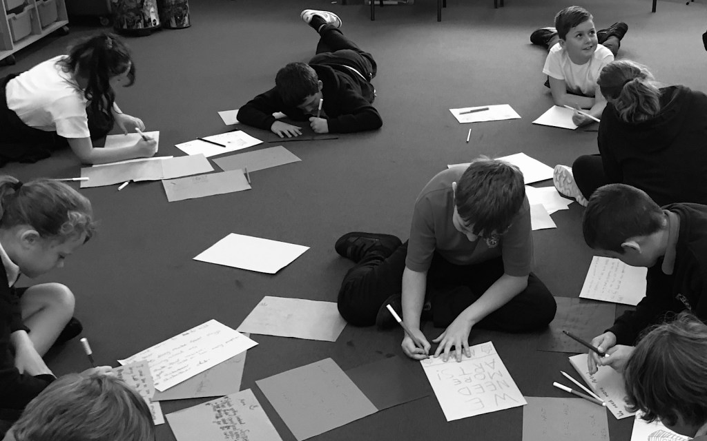 A monochrome image of students sitting on the floor writing on pieces of paper