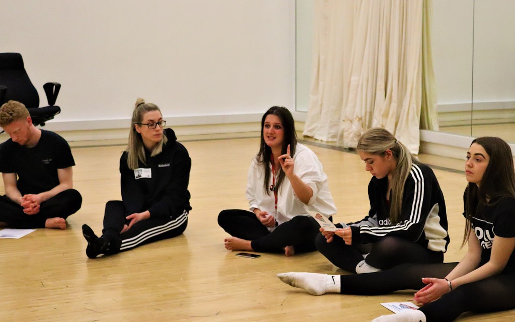 Young people and adult practitioners discuss a workshop whilst sitting in a circle