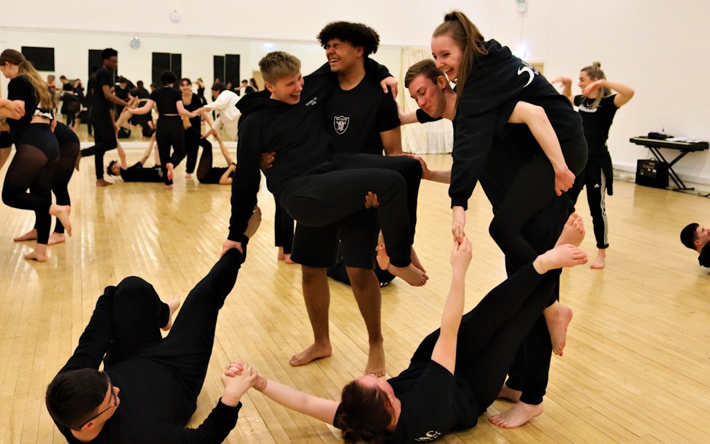 Dance students take part in a physical workshop during which some of them climb on the back of others whilst laughing