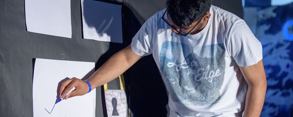 A young person stands by a wall and they are drawing a tick on a piece of paper on the wall