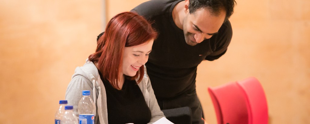 A member of theatre staff leans over a student and guides them about something they are reading on a piece of paper