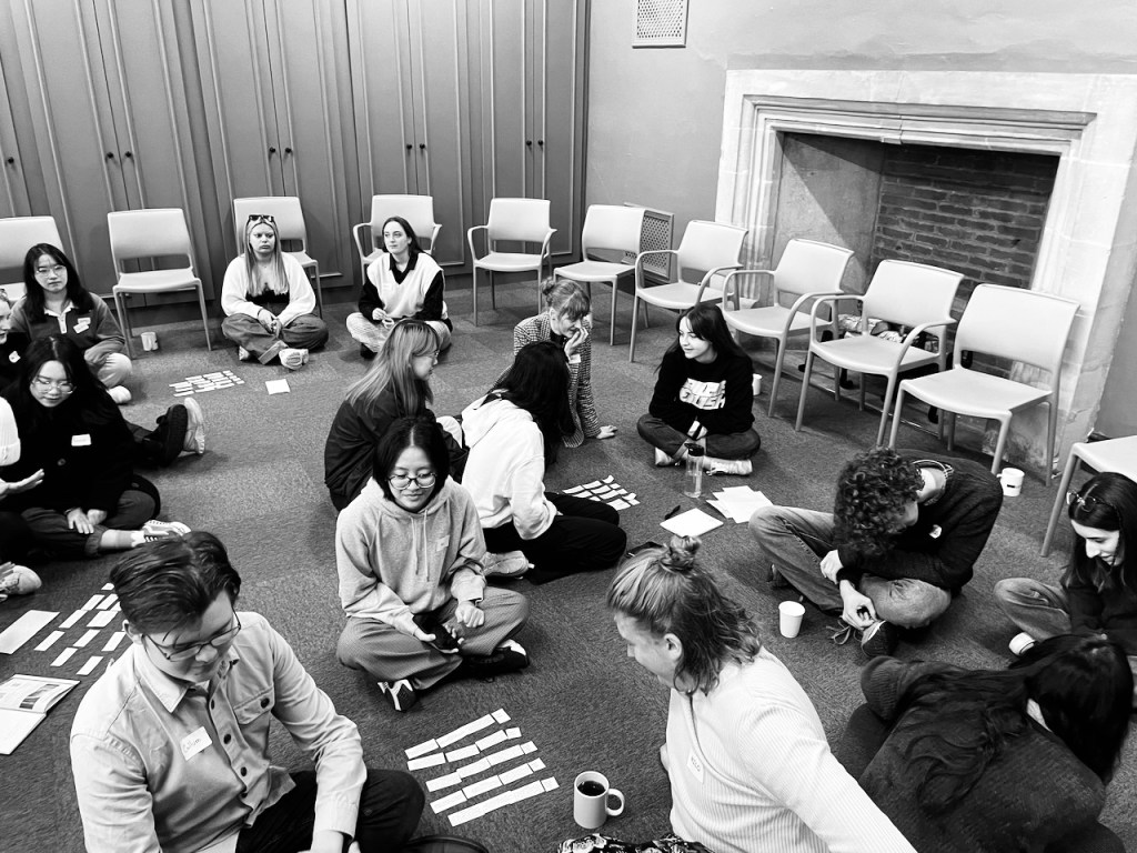 A large room of lots of students who sit on the carpet working in groups together