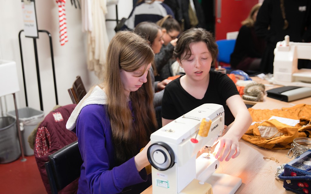 A student learns how to sew on a machine backstage in the costume department at a theatre