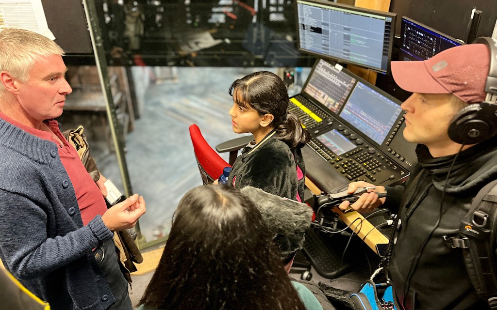 A behind the scenes tour at the Royal Shakespeare Company sees four people stand by a lighting desk