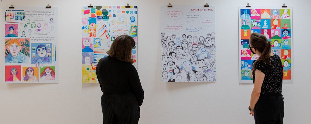 Two teachers look at art hung on a white wall