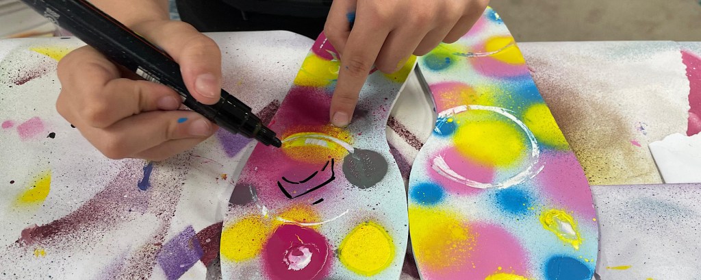 A child uses a black pen to draw on a piece of card shaped like a footprint