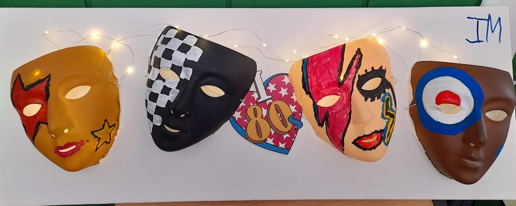 Four masks painted by students are joined together by fairy lights and in the middle is a graphic which says I heart 80s