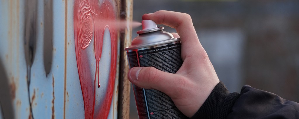 A child uses a spray can of red paint on a wall