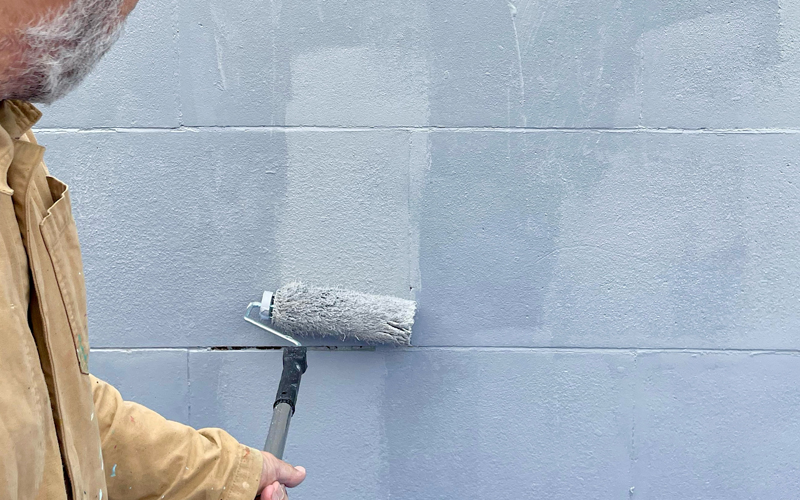 An artist uses a roller to paint an outside wall grey