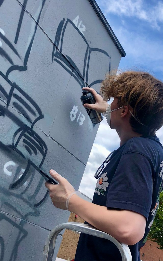 An artist is spray painting a book symbol on a library