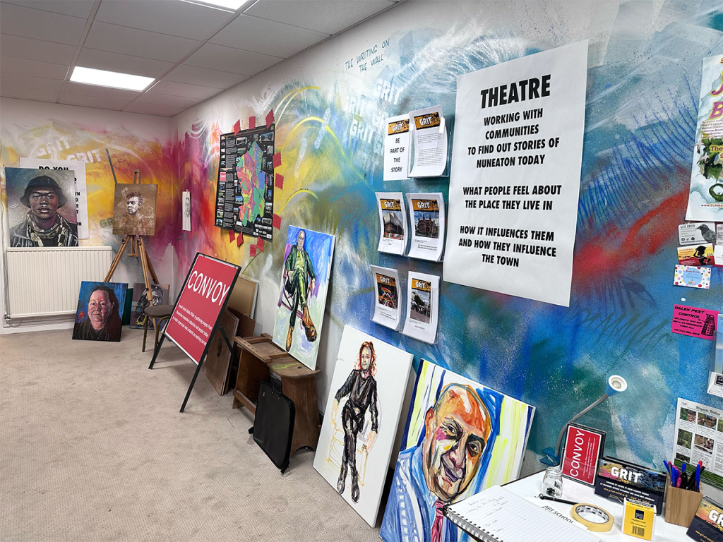 A wall in an art gallery is decorated brightly and has signs on it as well as other artwork