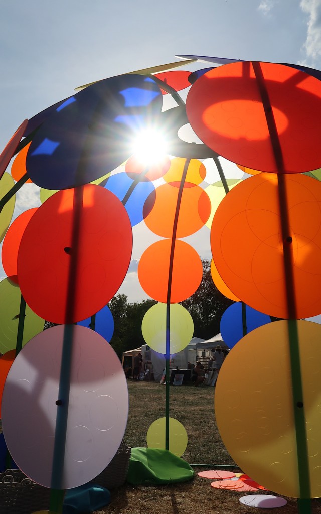 A large dome outside at a festival is made from colourful dots of colour