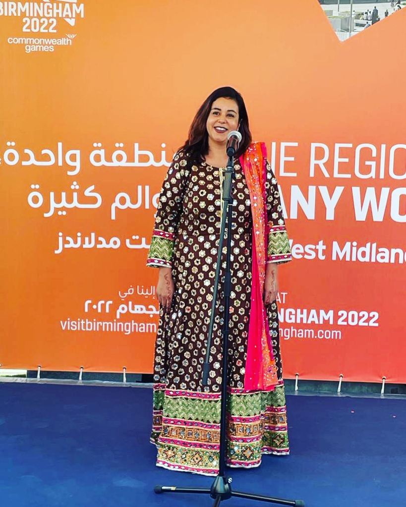 A writer stands at a microphone in front of an orange background at an event