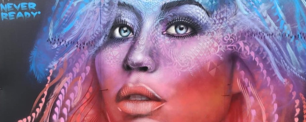 A woman’s face in spray paint is blue, red, pink and purple