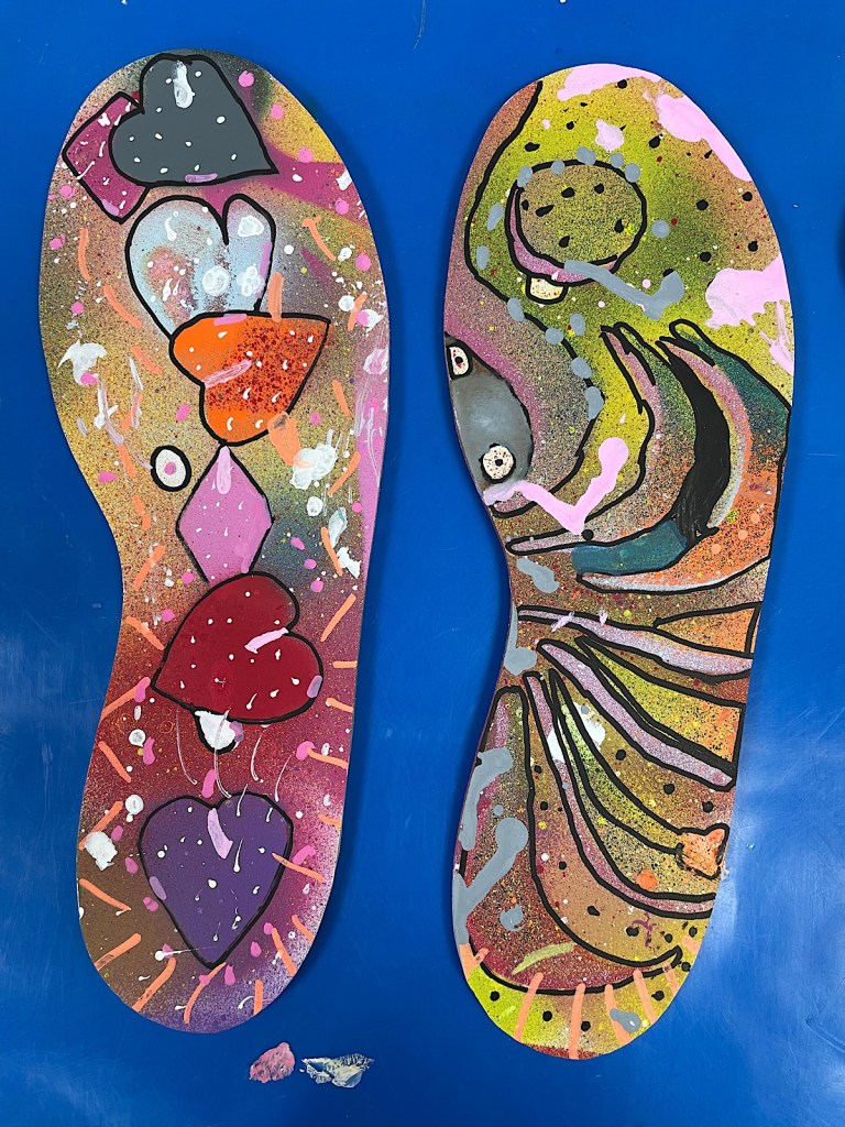 Two footprint shaped pieces of card decorated with colours and patterns including hearts, diamonds and stripes