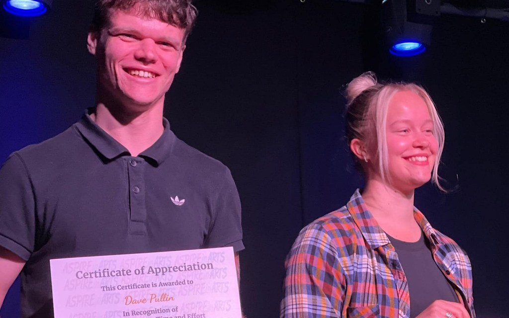 Two young people stand on a stage and smile and they are holding certificates