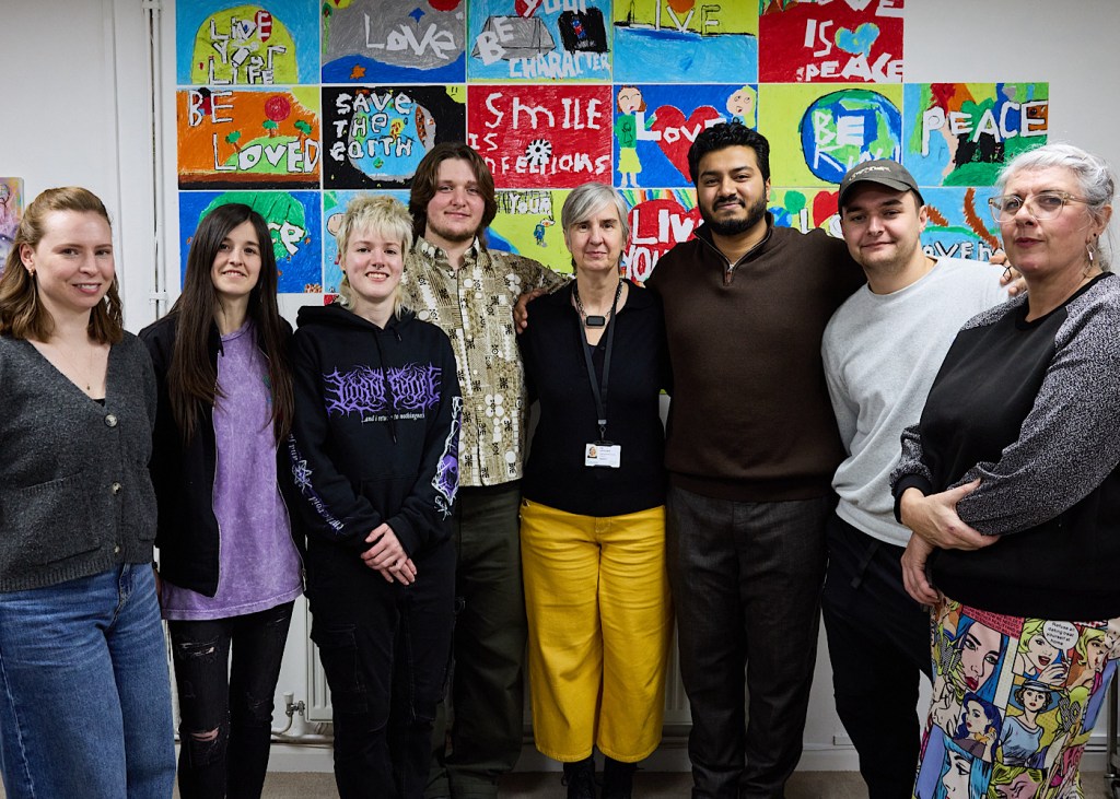 Eight people stand in a line in front of a wall of paintings