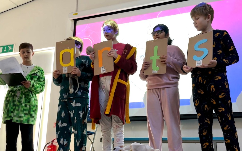 Four students hold clipboards with letters on which spell out the word arts