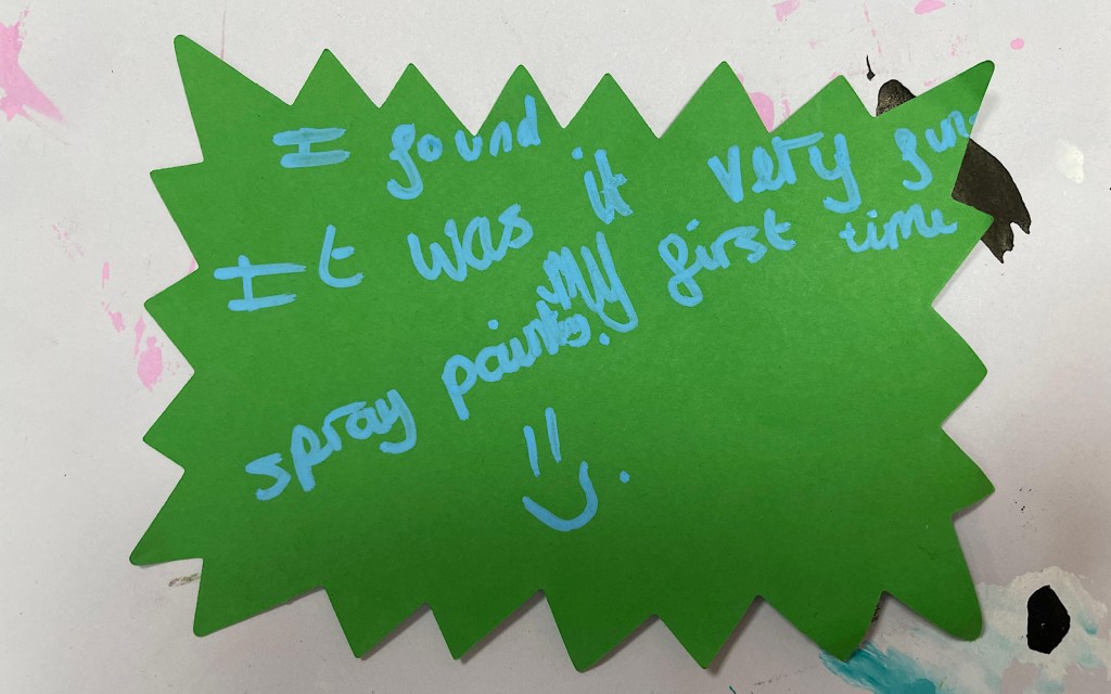 A child has written on a piece of green card “I found it was very fun, my first time spray paints”
