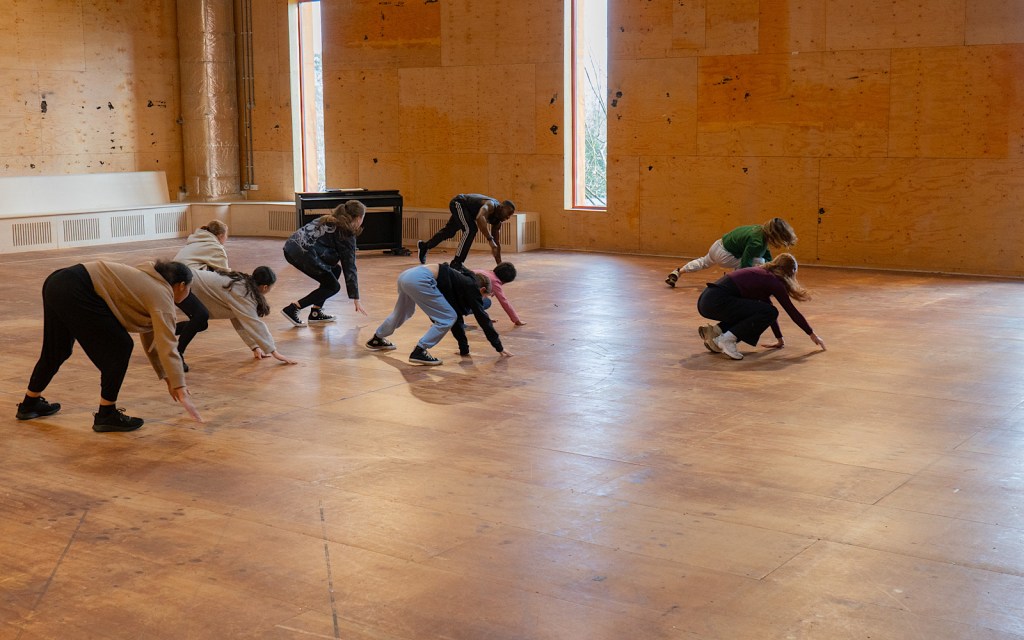 Students create dance as part of a workshop in a large room with wooden walls and floor