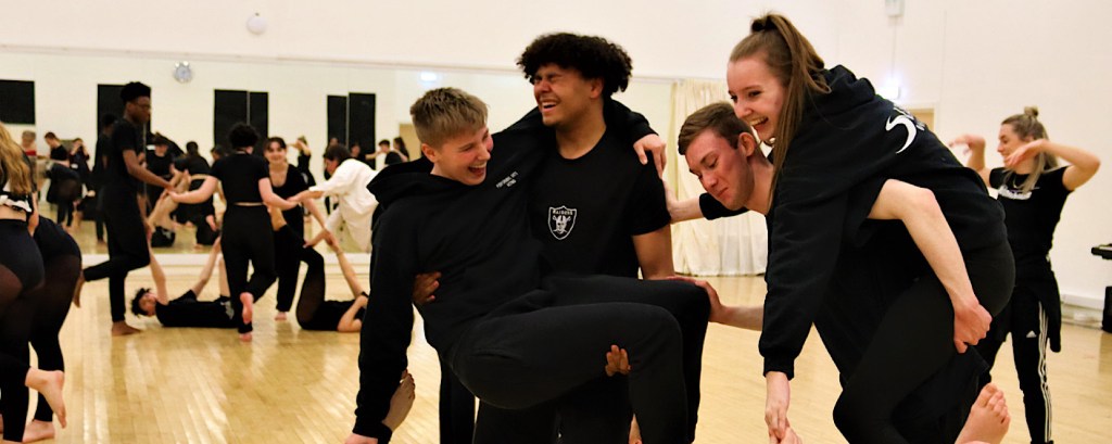 Dance students take part in a physical workshop during which some of them climb on the back of others whilst laughing