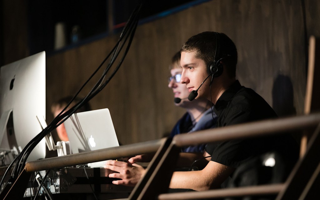 A student wearing headphones is learning about how to operate sound and lighting on a stage