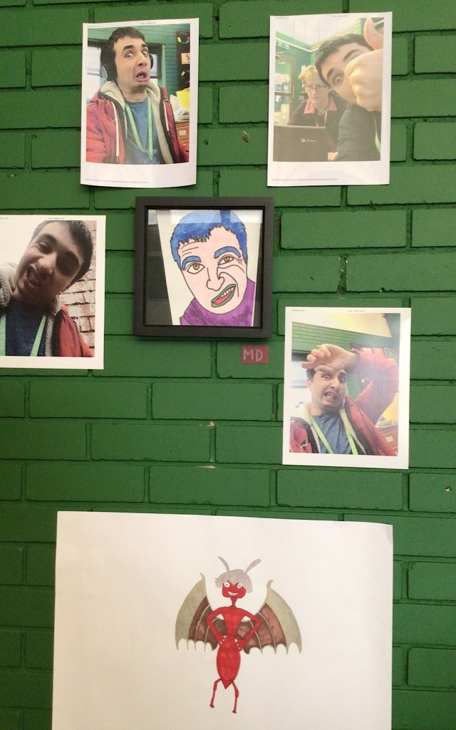 On a green wall are some selfie photographs taken by a student as well as a drawn portrait of someone with blue hair and green lips