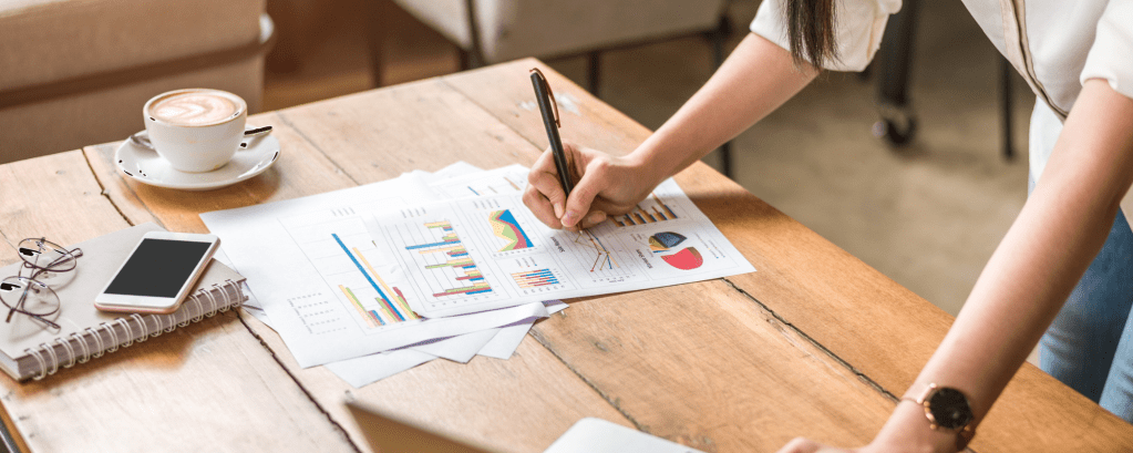 Someone leans over a desk and writes on reports that include graphs