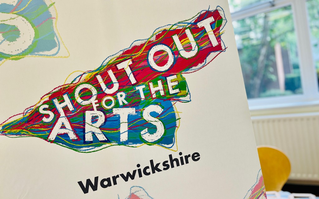 A banner at a fair says ‘shout out for the arts’