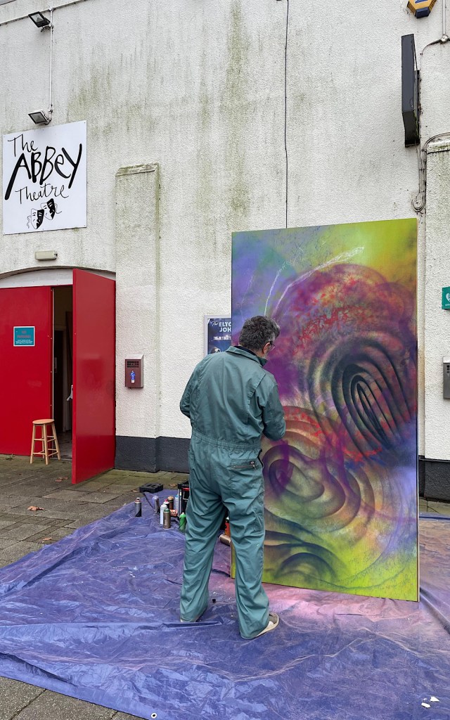 An artist in overalls spray paints a huge mural outside a theatre in Nuneaton