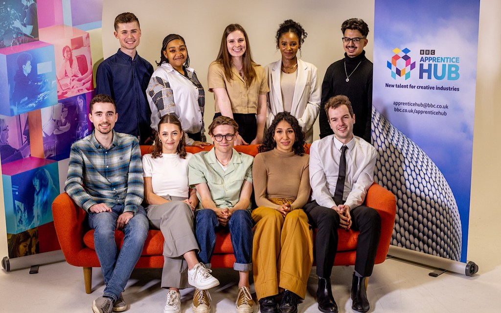 Two rows of apprentices look to the camera, at the front they sit on a red couch