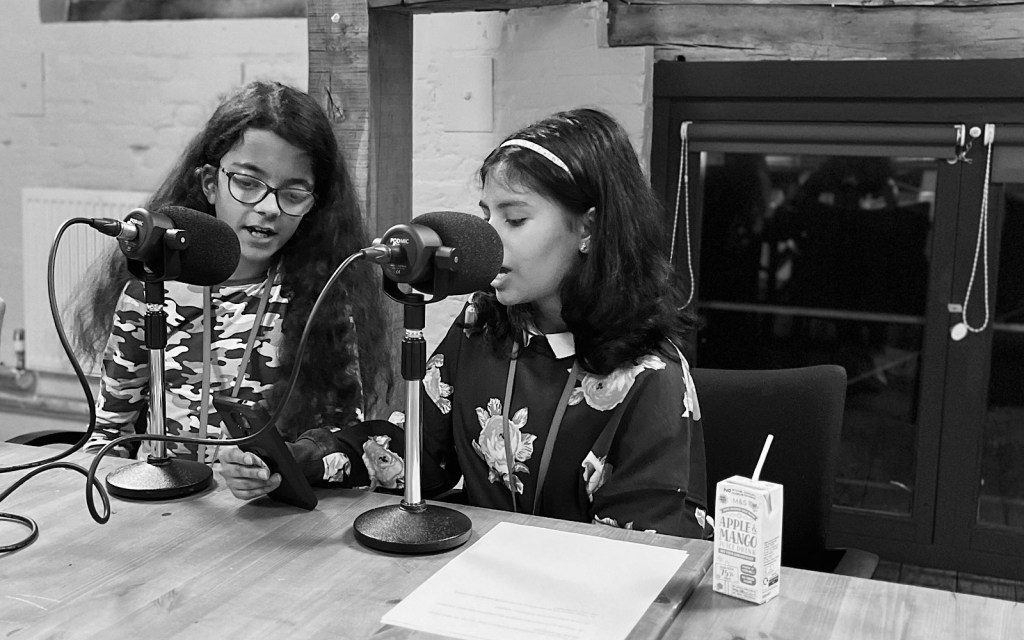 Two students talk into two microphones as part of a podcast recording
