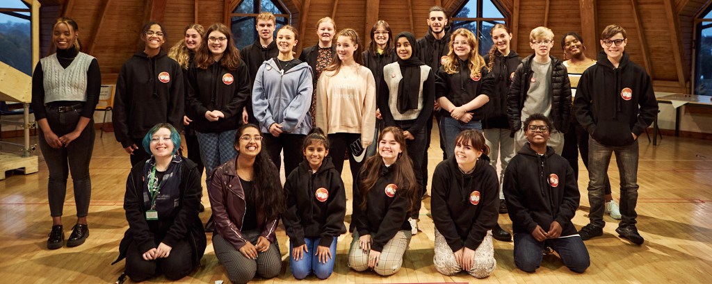 A group of young people stand for a group photo and they all look to the camera and smile