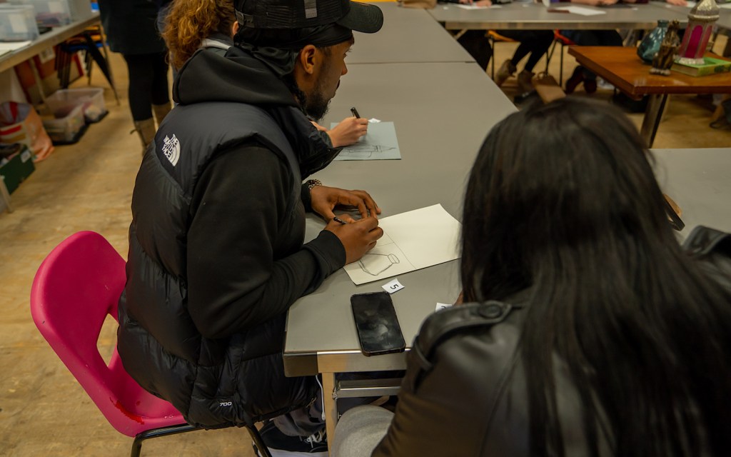 Two people draw on paper as part of an arts workshop