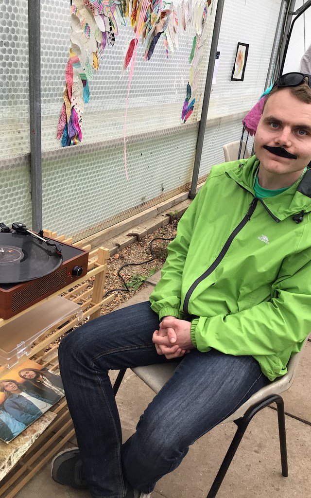 A student in a green jacket sits by a record player outside