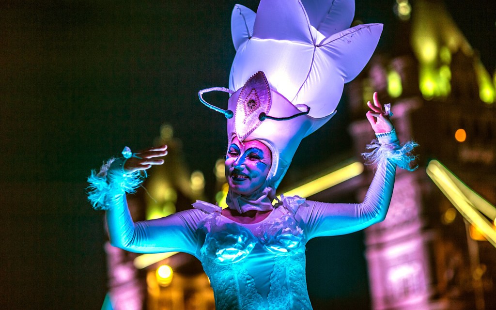 A performer wears a bright purple costume which includes a large headpiece that looks like a flower
