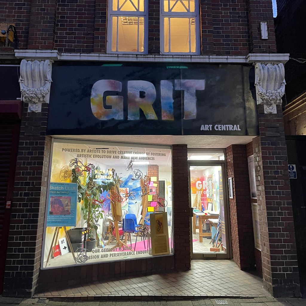 The outside of a shop at night on a high street, the sign reads ‘GRIT’
