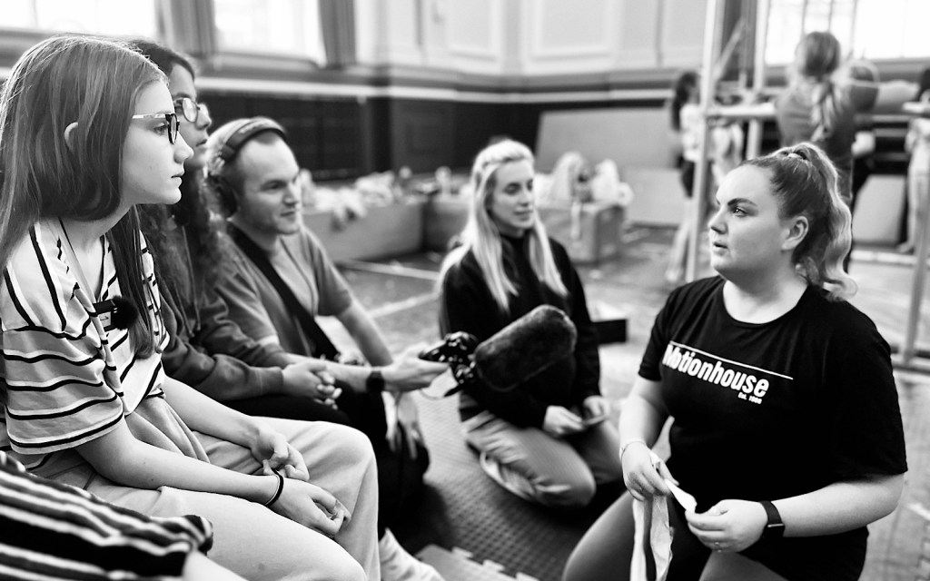 A group of people face a dancer who is wearing a t-shirt which says ‘Motionhouse’ on it