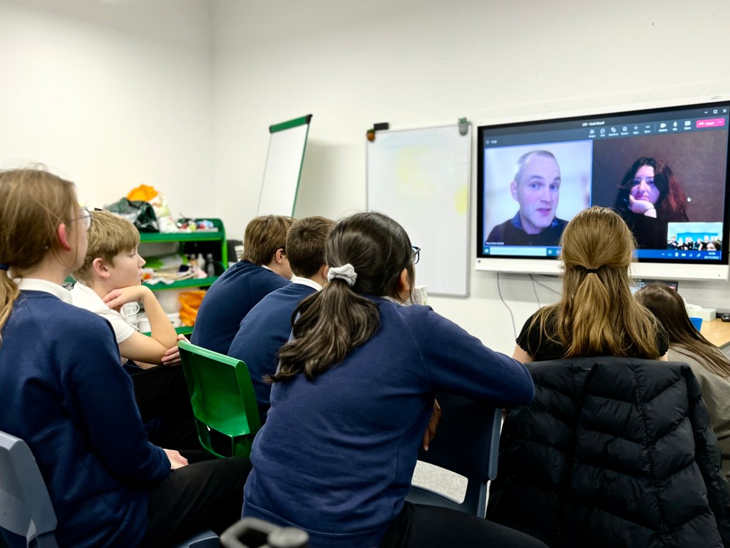 Students look at a screen in a classroom which has two faces on it