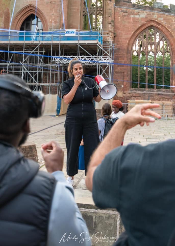 A writer stands in front of people talking in a megaphone outside