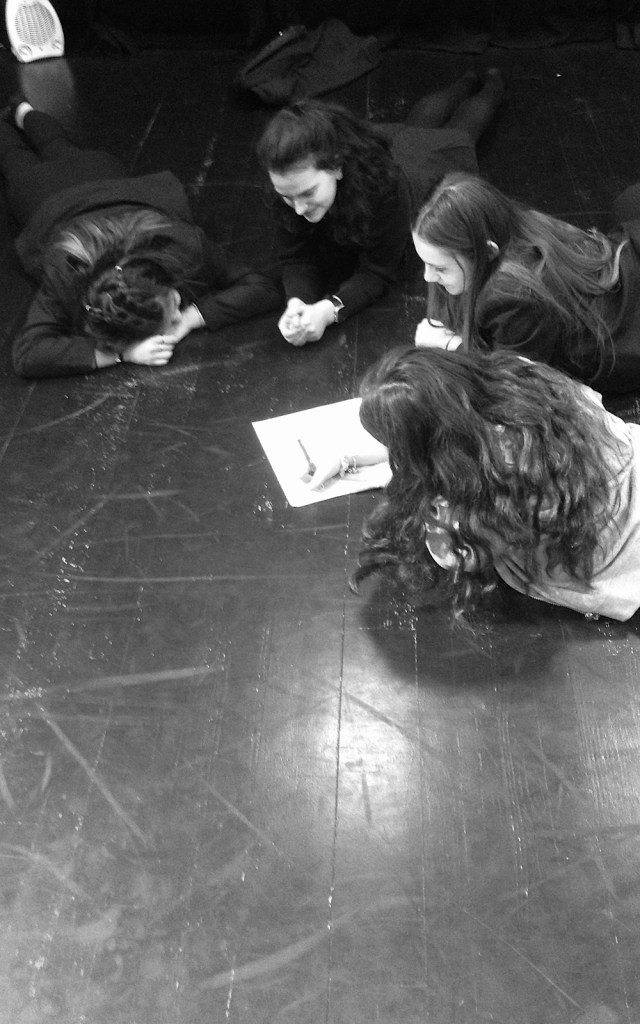 Four students lie on the floor writing on a piece of paper