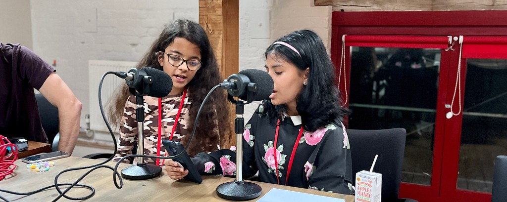 Two students talk into two microphones as part of a podcast recording