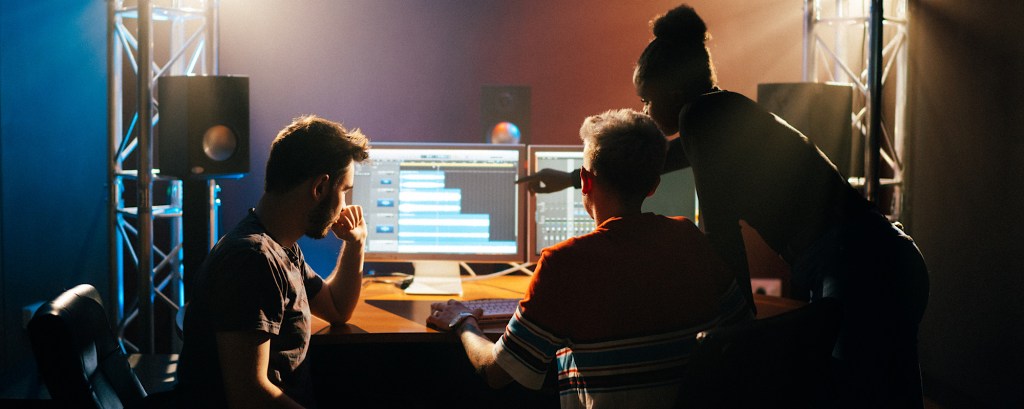 Three students look at work on a screen in a studio