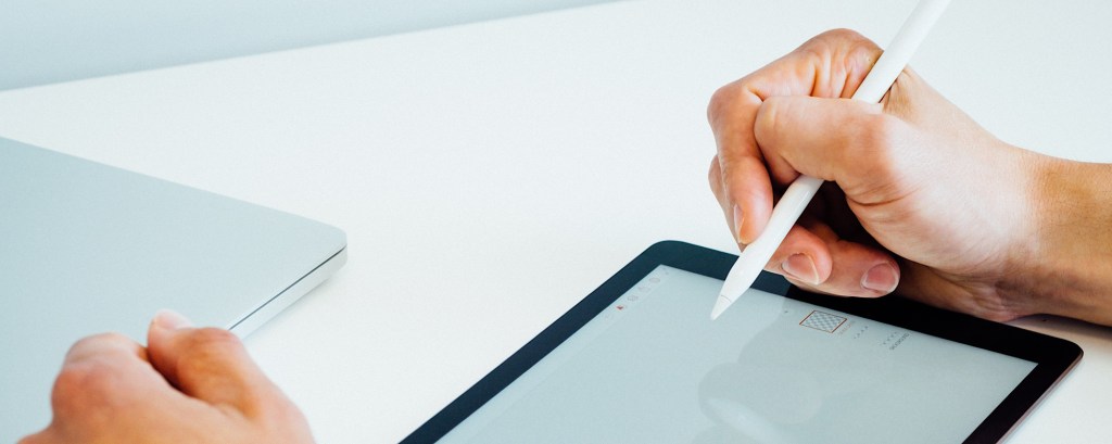 A graphic designer holds an Apple Pencil as they design a logo on an iPad