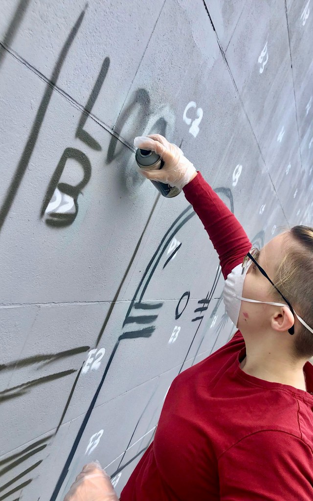 A artist wears a mask as they are using a spray paint can to create graffiti