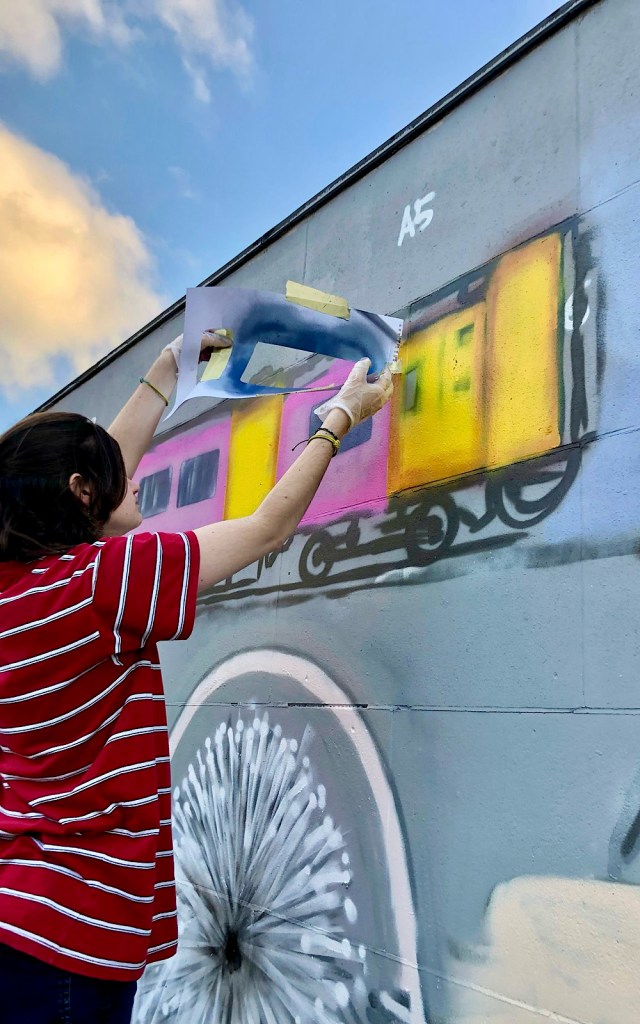 A young artist is painting a train on the side of a building