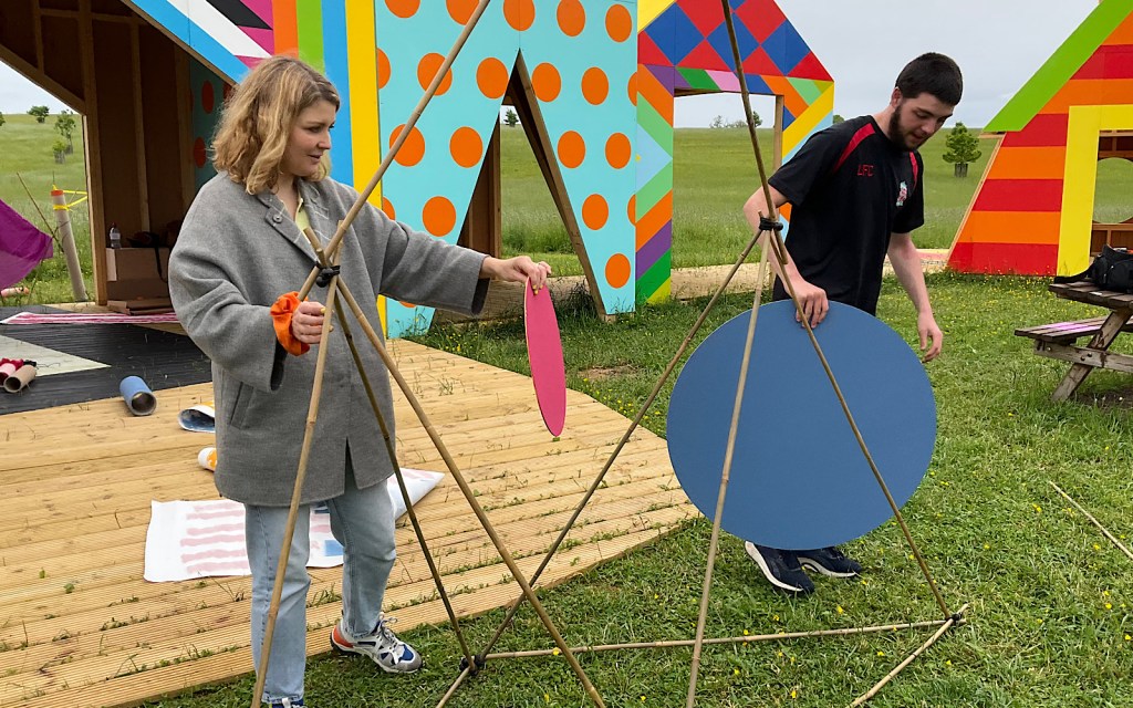 Two people are using sticks and shapes to construct something in a field