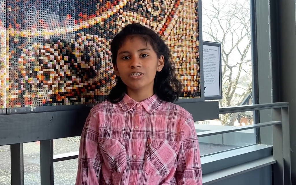 A young student wearing a pink shirt looks at the camera and talks to it