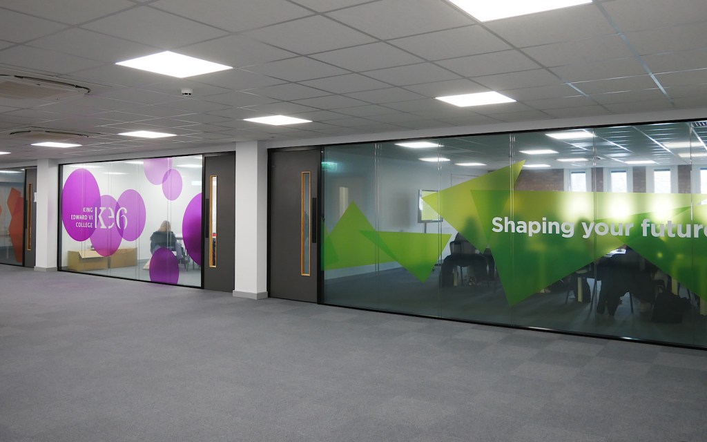 Inside a college, two rooms filled with seats can be seen behind glass walls