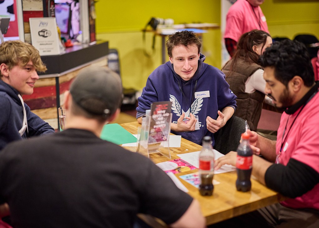 Four young people sit and eat lunch at a table and talk to each other